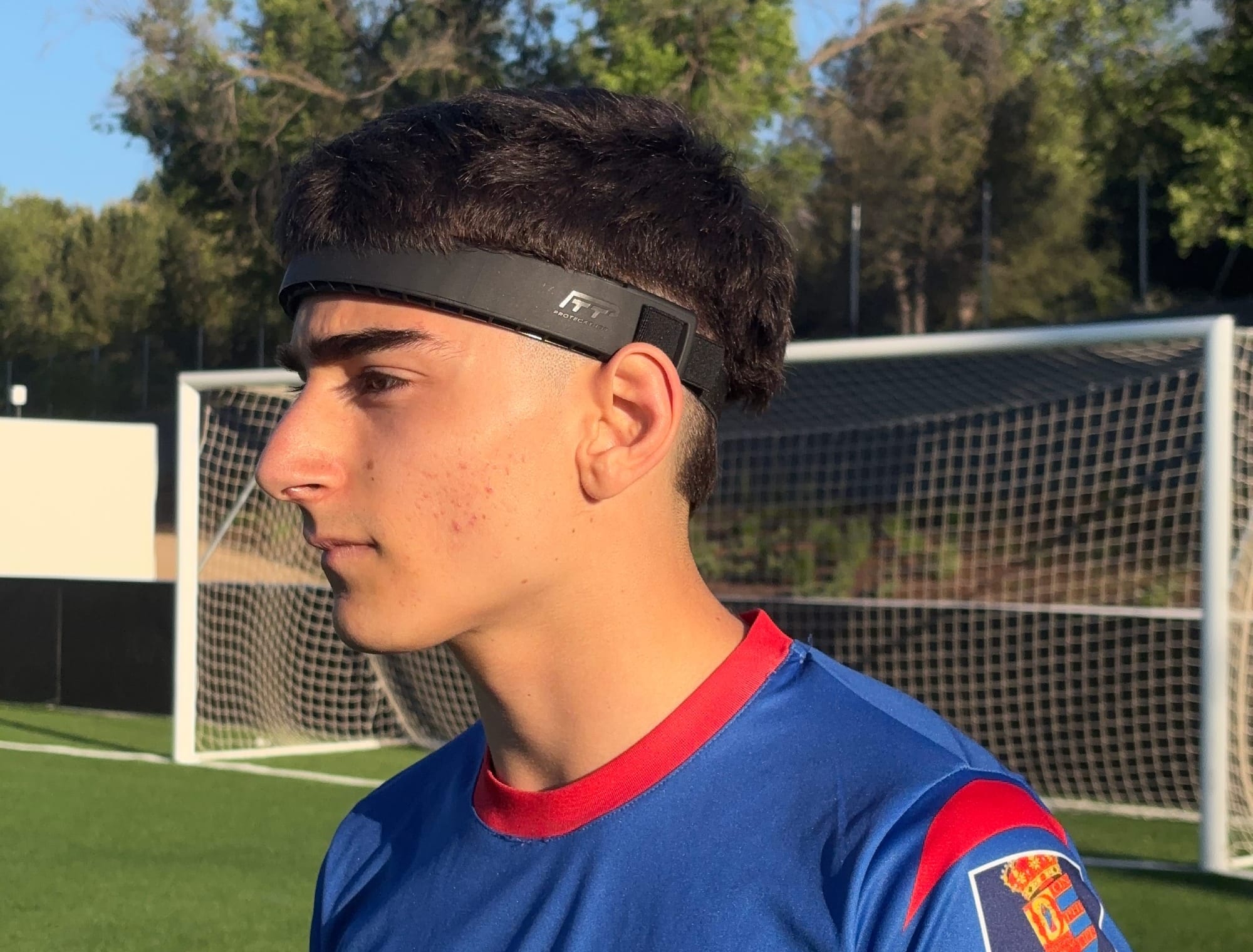 “Futbolista profesional en el campo con expresión reflexiva, usando cinta protectora Proteckthor para evitar impactos en la cabeza.”